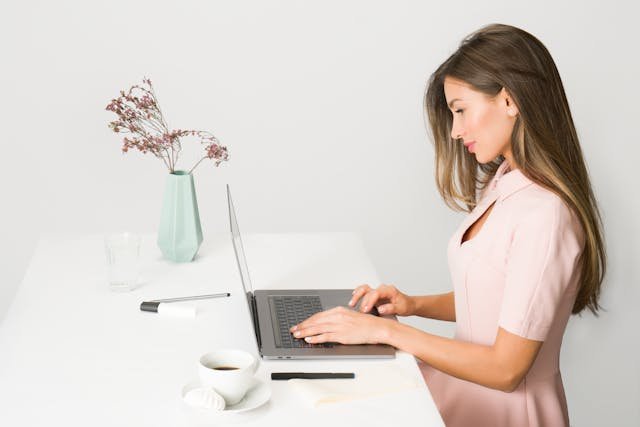 freelancer writing on her laptop with a a green vase of flower