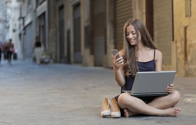 freelancer sitting on a pavement looking at her phone